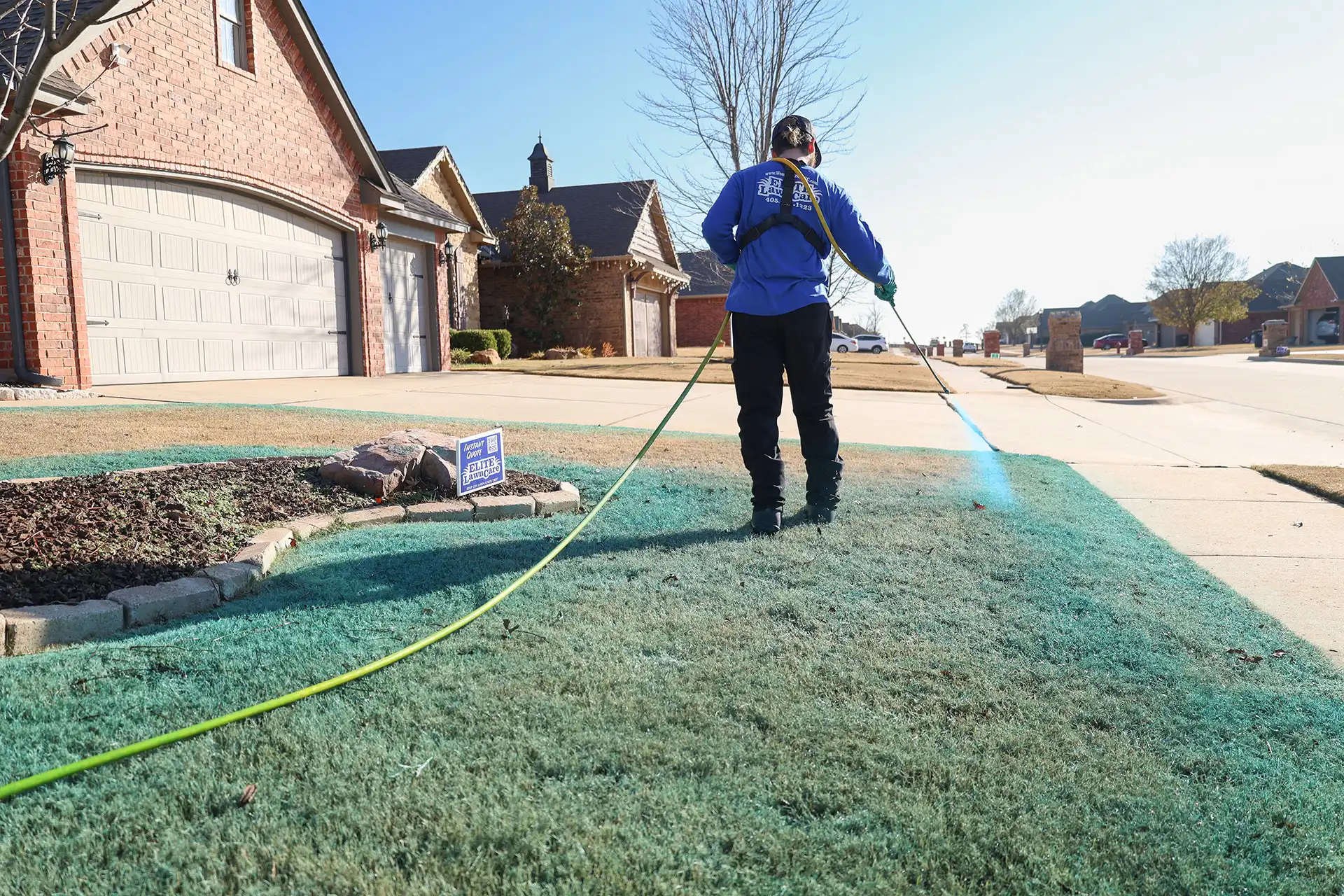 Lawn care technician spraying green liquid treatment on a residential front yard