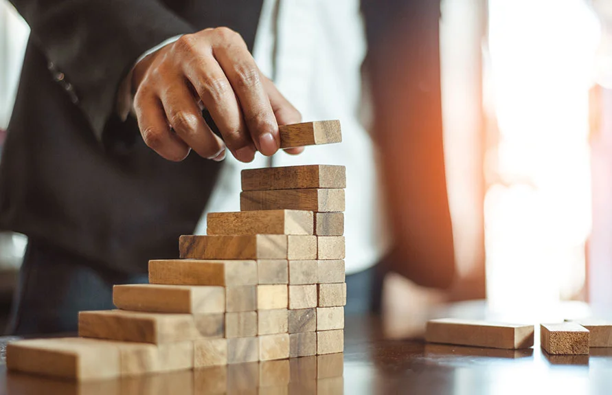 Hand in a suit stacking wooden blocks into steps, a symbol of business formation planning