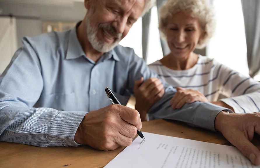 Smiling older couple signing estate planning documents at a table