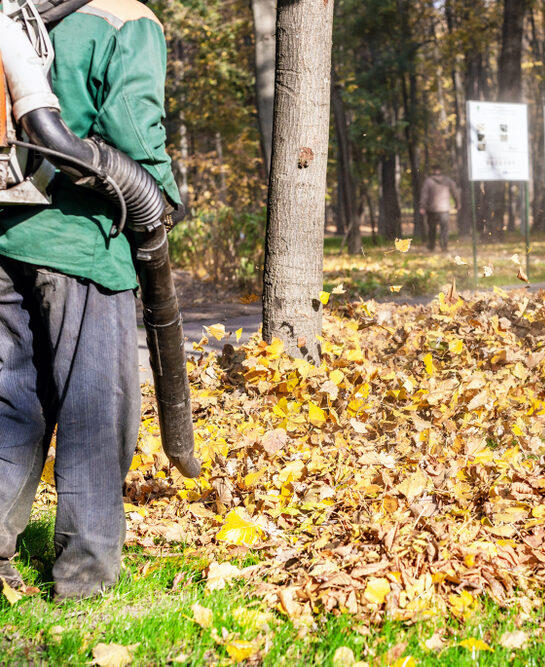 Keast crew member clearing fallen leaves with a backpack blower