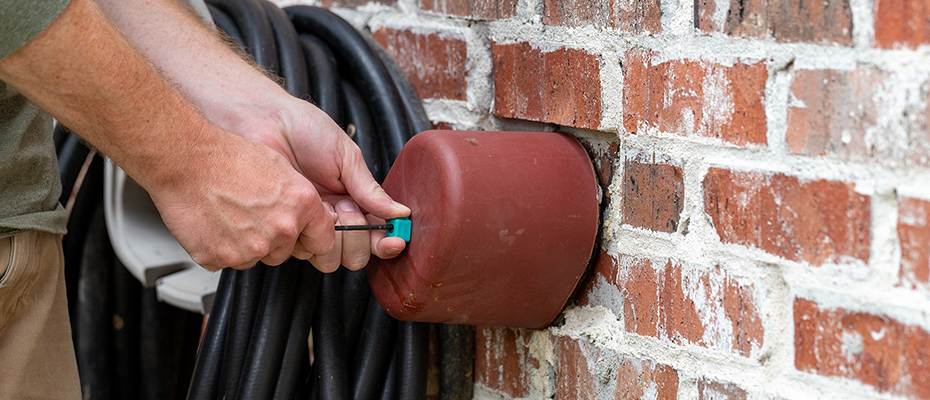 Technician connecting an air hose to an irrigation fitting on a brick wall for a winter blowout