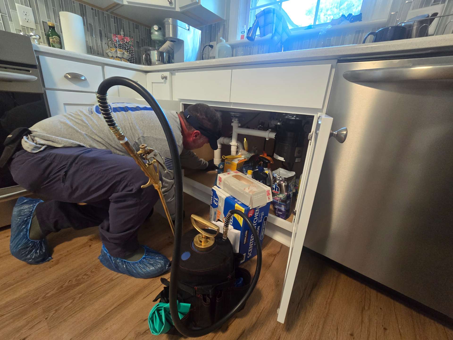 Pest control technician with a sprayer inspecting under a kitchen sink cabinet