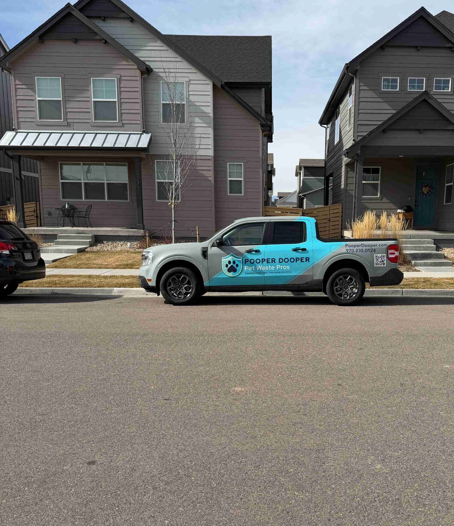 A Pooper Dooper service truck parked on a residential street in front of a home