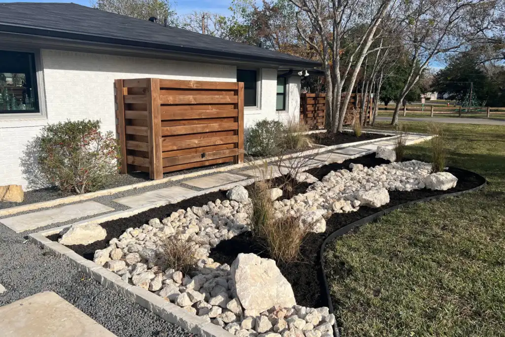 Modern front yard landscaping with a dry creek rock bed and wood fence