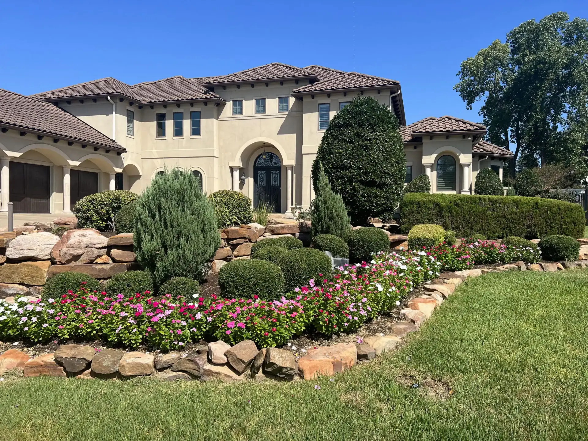 Mediterranean-style home with landscaped stone flower beds and manicured shrubs
