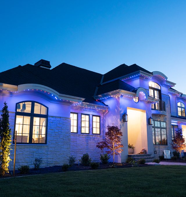 Warm white roofline display on a two-story East Brainerd home at dusk with neighbors' houses lit along the street, by New Age Lights