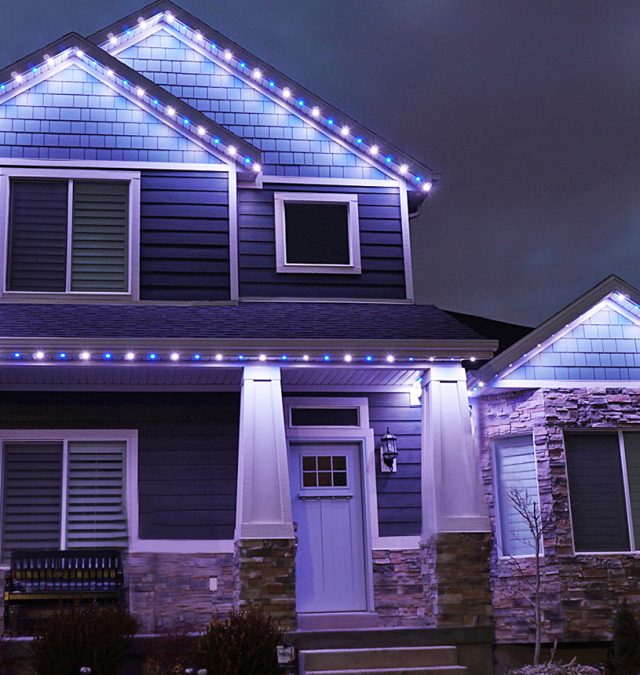 A two-story Fairfield, Ohio home lit in red and green permanent roofline lighting with snow on the lawn, installed by New Age Lights