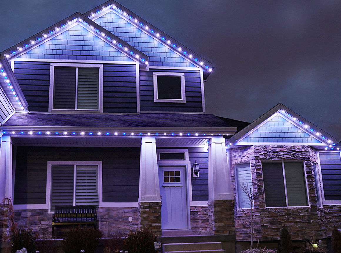 Two-story home at night with blue and white permanent lighting along the rooflines and gables