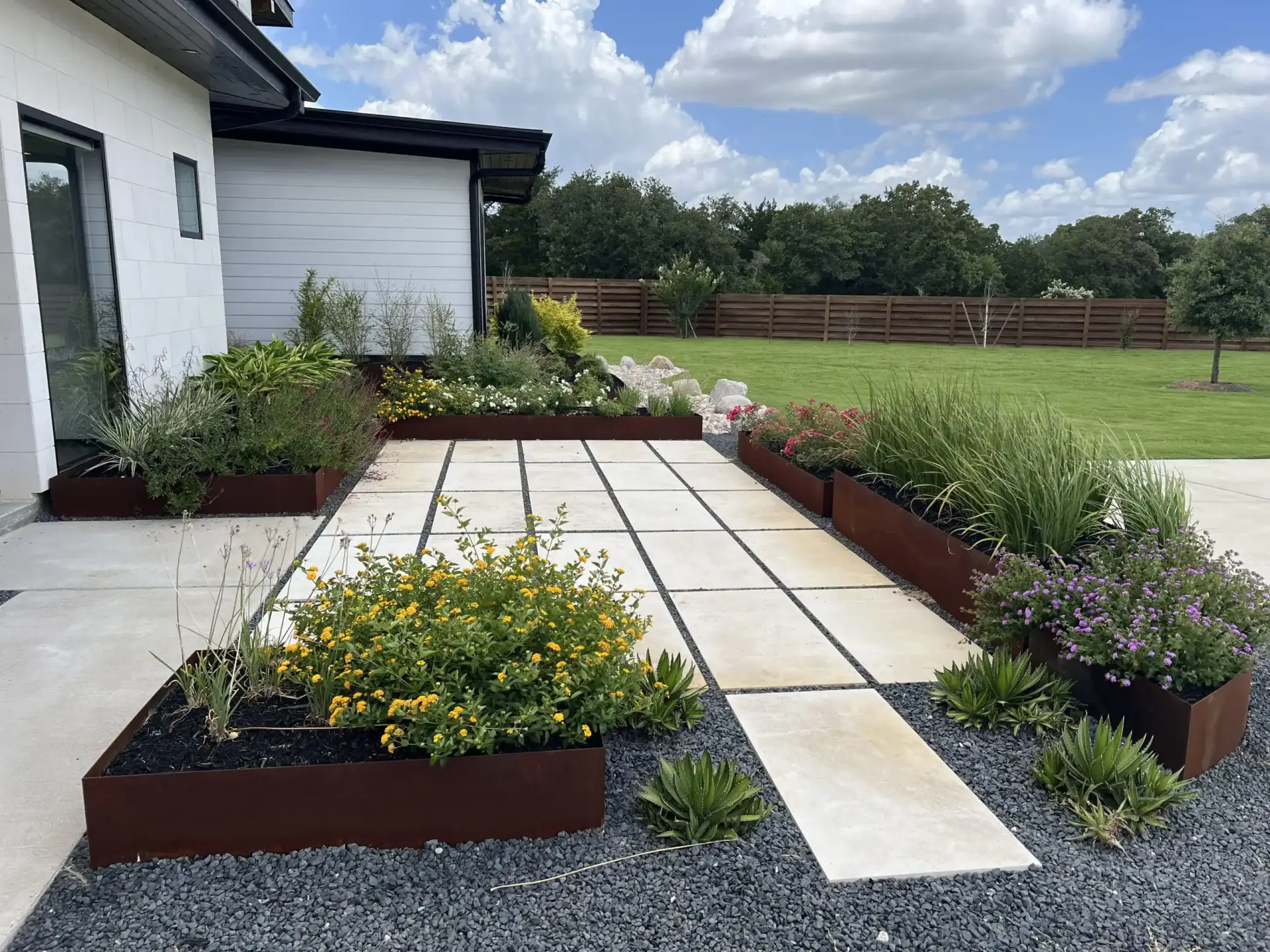 Paver terrace framed by raised steel planters full of flowering plants