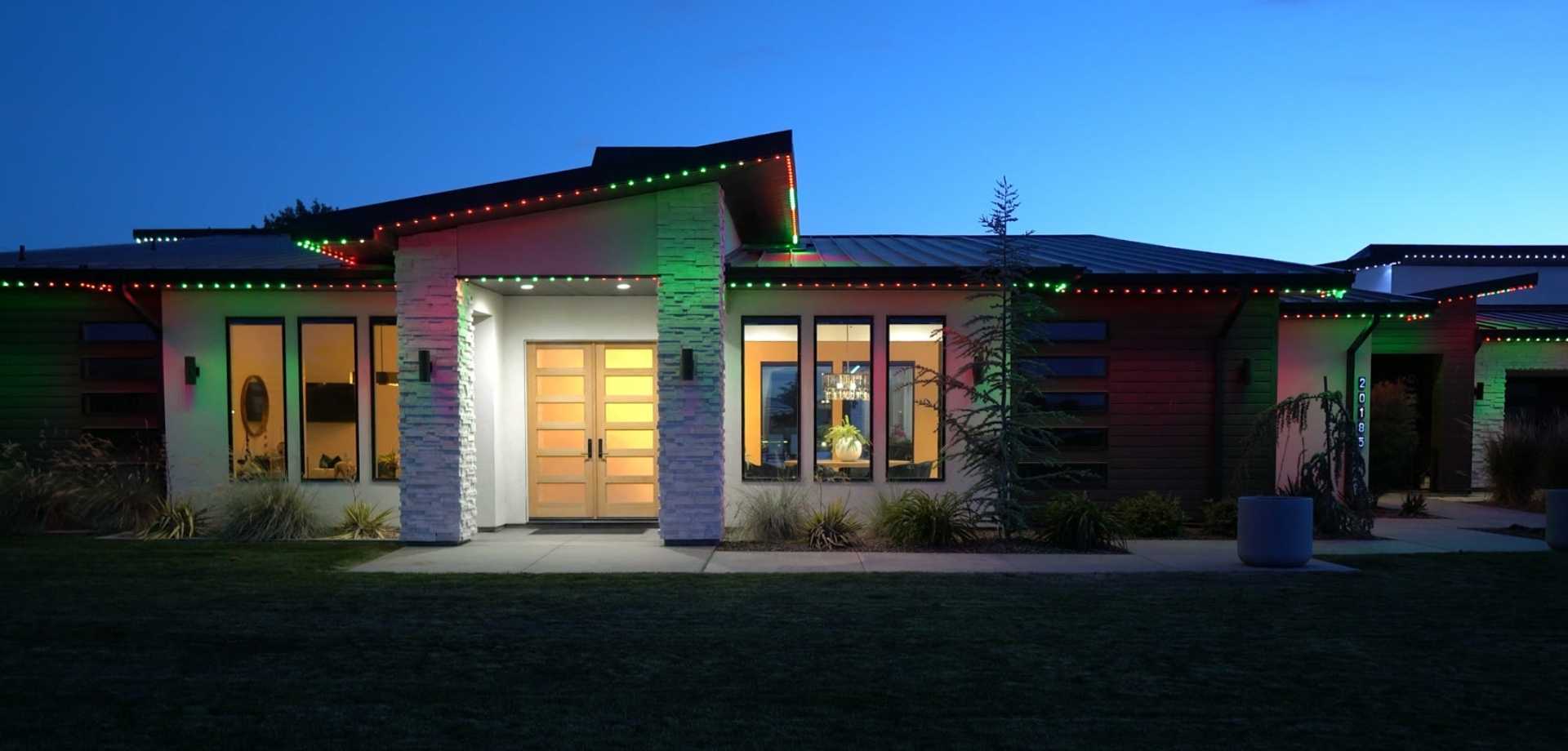 Modern single-story home at dusk with red and green permanent lighting along the rooflines