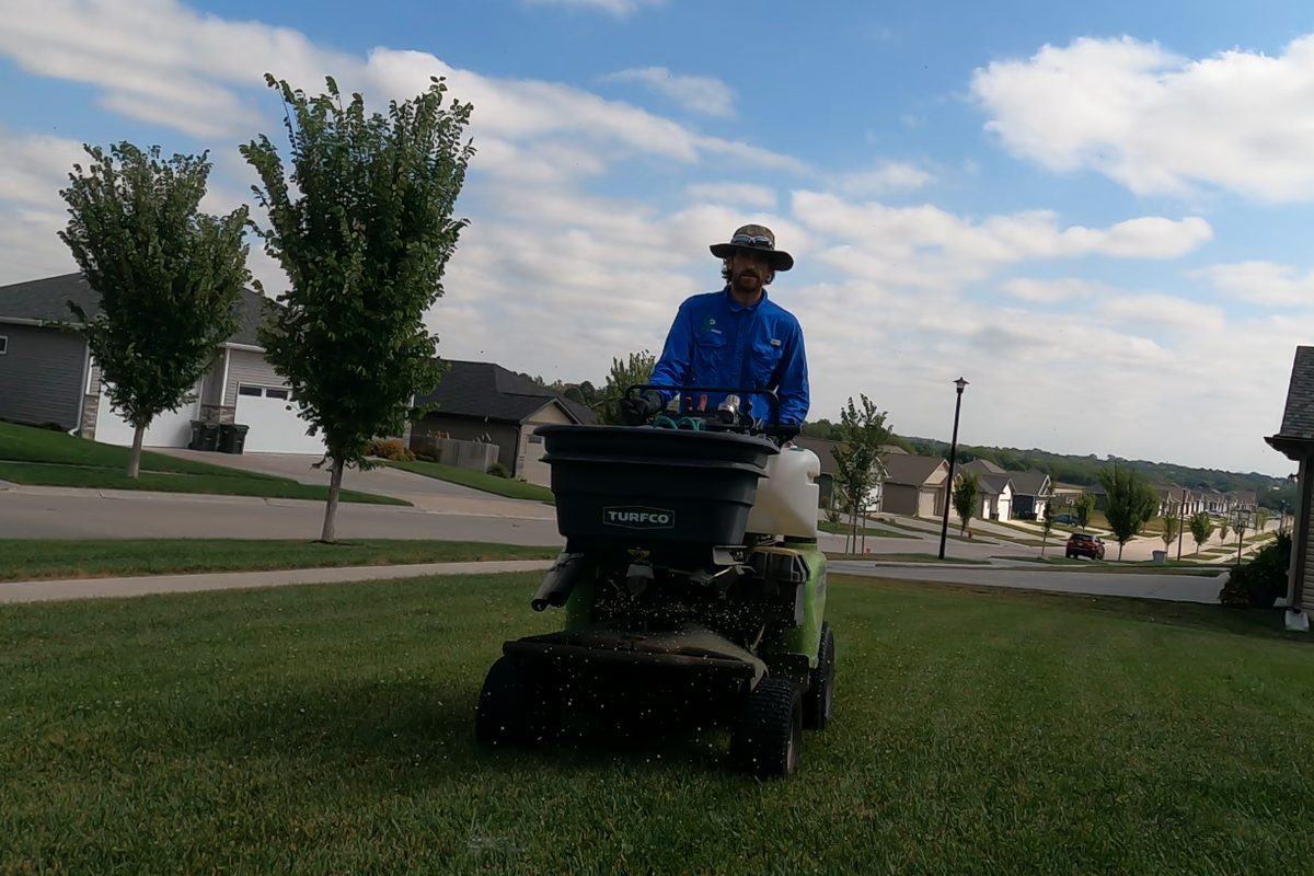 A Yard Boss team member applying fall fertilizer to a lawn with a ride-on spreader