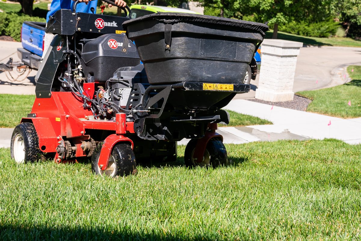 A close-up of a Yard Boss core aerator pulling plugs from a green lawn