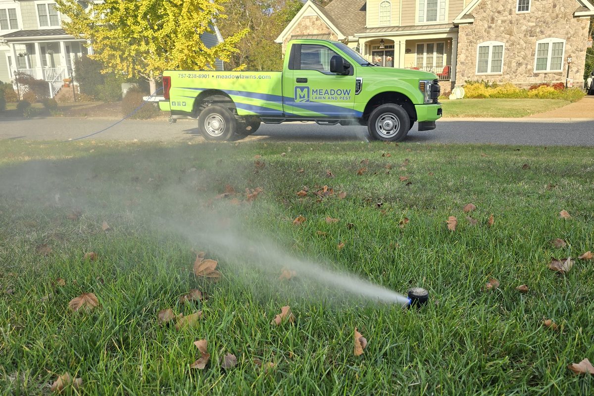A Meadow Lawn and Pest truck at a home with a sprinkler running before a winter blowout