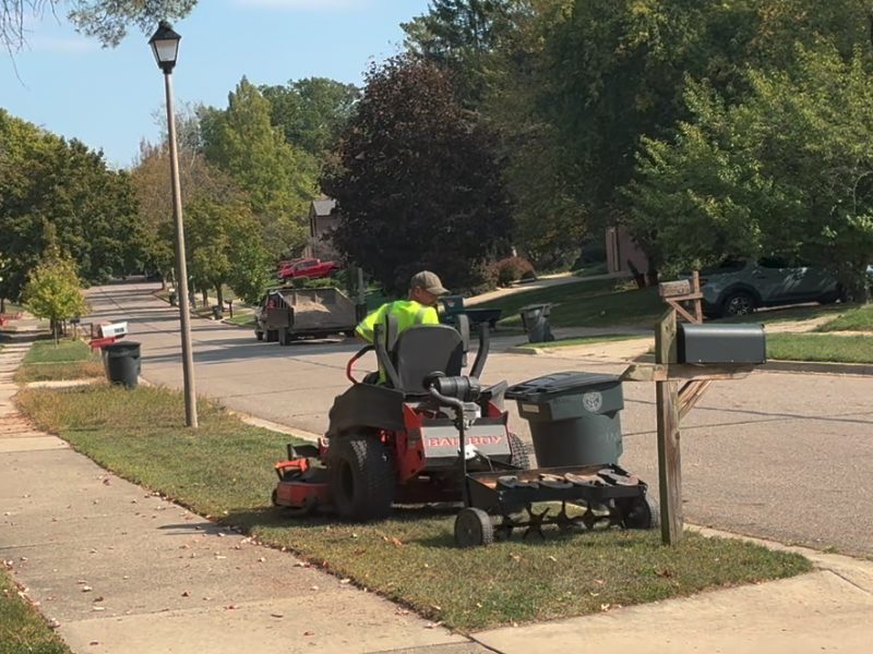 Fresh grass seed being spread over a freshly aerated East Lansing lawn in fall