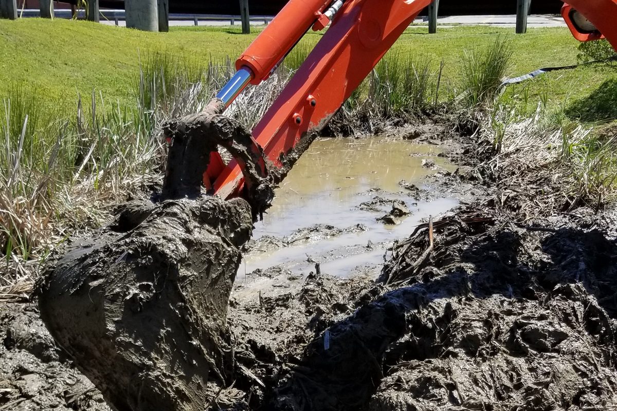A Kubota excavator digging a drainage trench to solve standing water in a Richmond-area yard