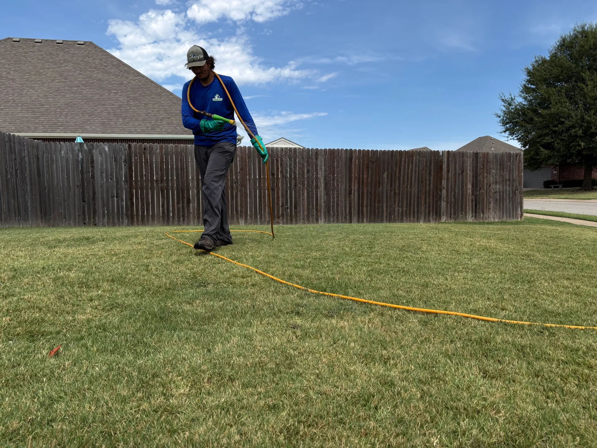 Fall Armyworms and Grubs: Protecting Your Tulsa Lawn from Fall Pests Complete Lawn Care technician spraying a lawn with a hose along a backyard fence