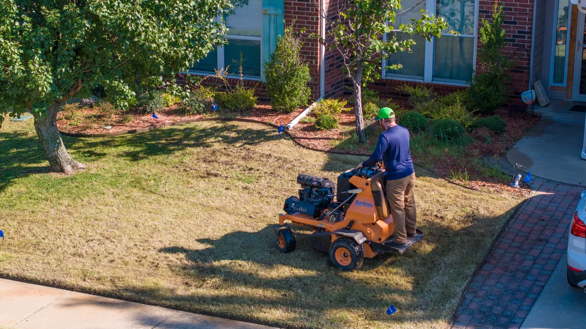 Complete Lawn Care technician aerating a front lawn with a stand-on aerator