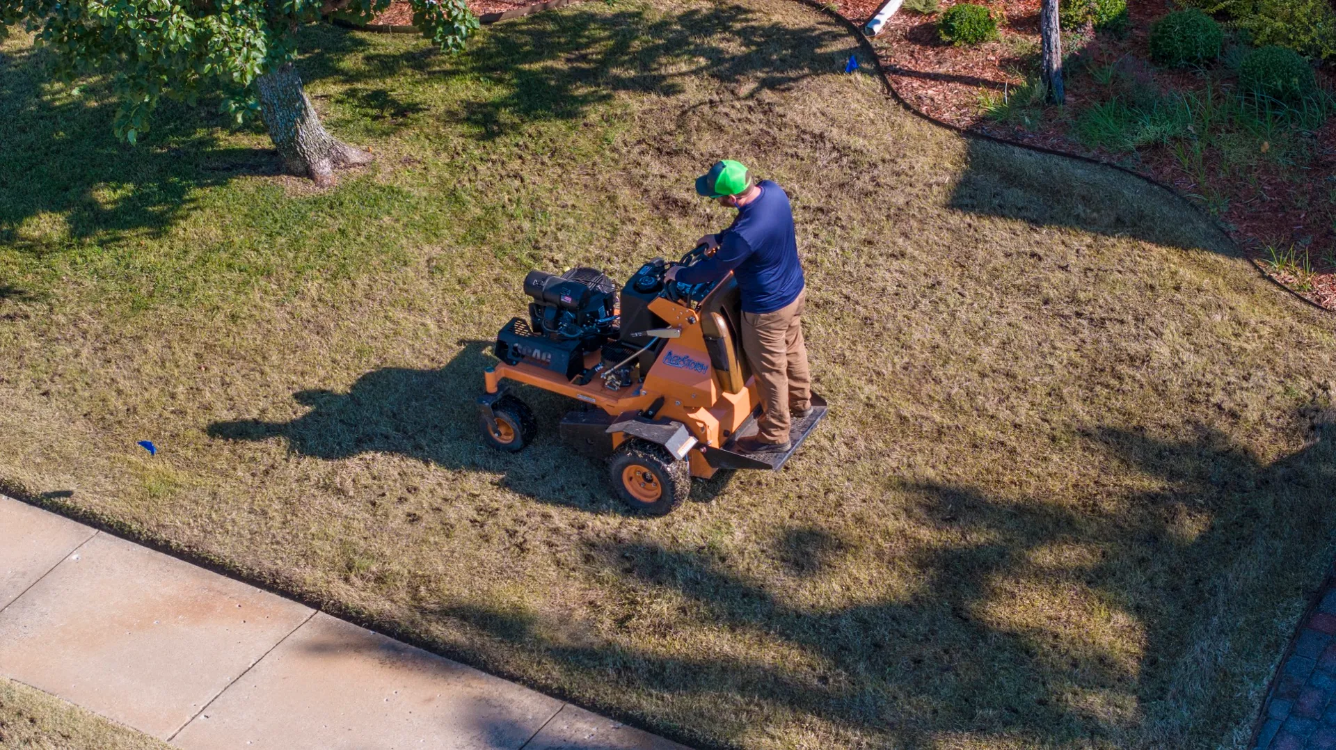 Complete Lawn Care technician running a stand-on aerator across a dormant lawn