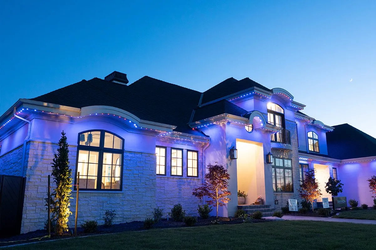 Large stone home at dusk with blue permanent lighting along every roofline
