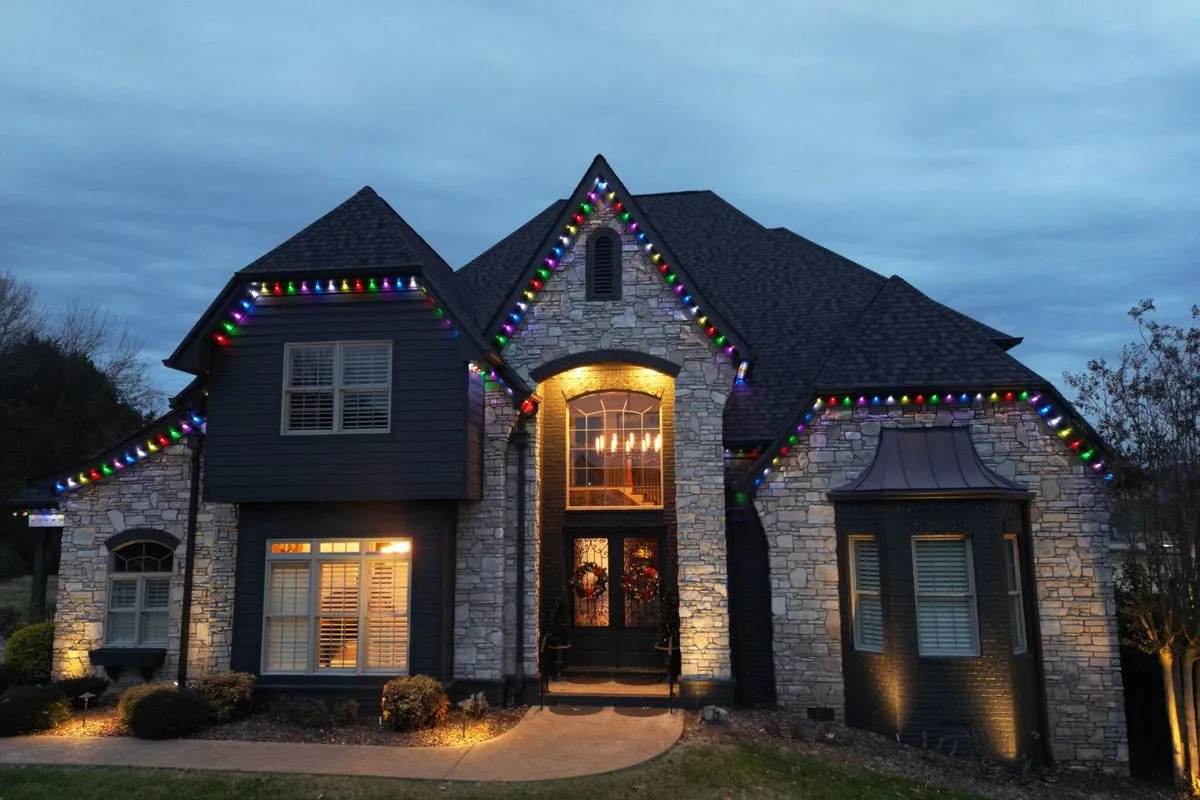 Stone and dark-sided home at dusk with multicolor lights along its steep gables