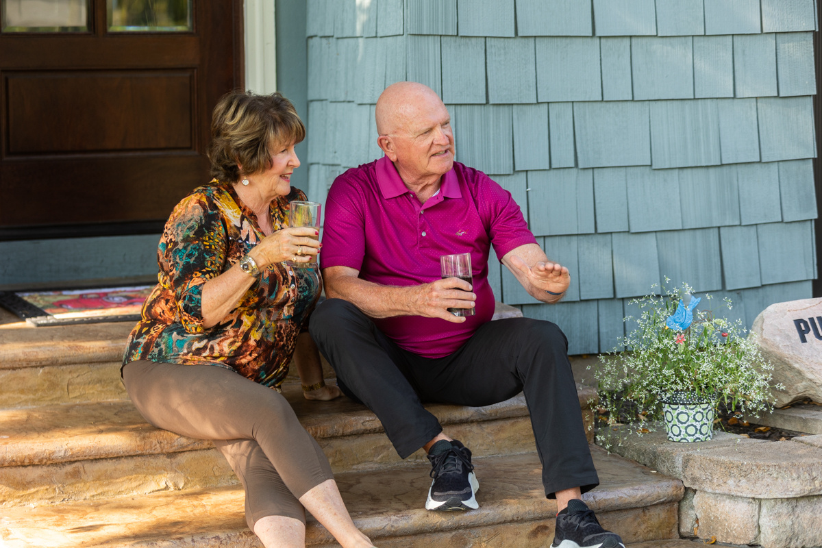 Older couple relaxing with drinks on the front steps of their home