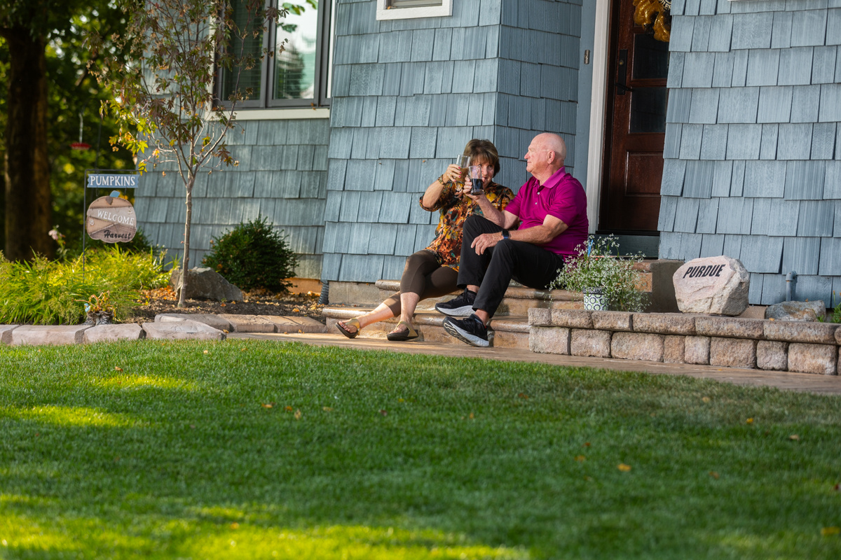 Couple sitting on the front steps of a blue-sided home above a green lawn