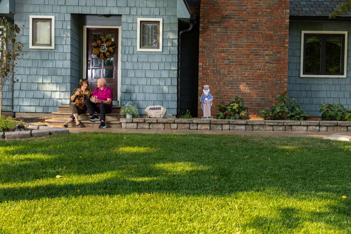 Wide green front lawn of a blue-sided home, with a couple sitting on the porch steps