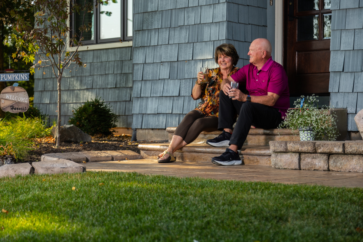 Couple toasting on the front steps of their home beside a green lawn