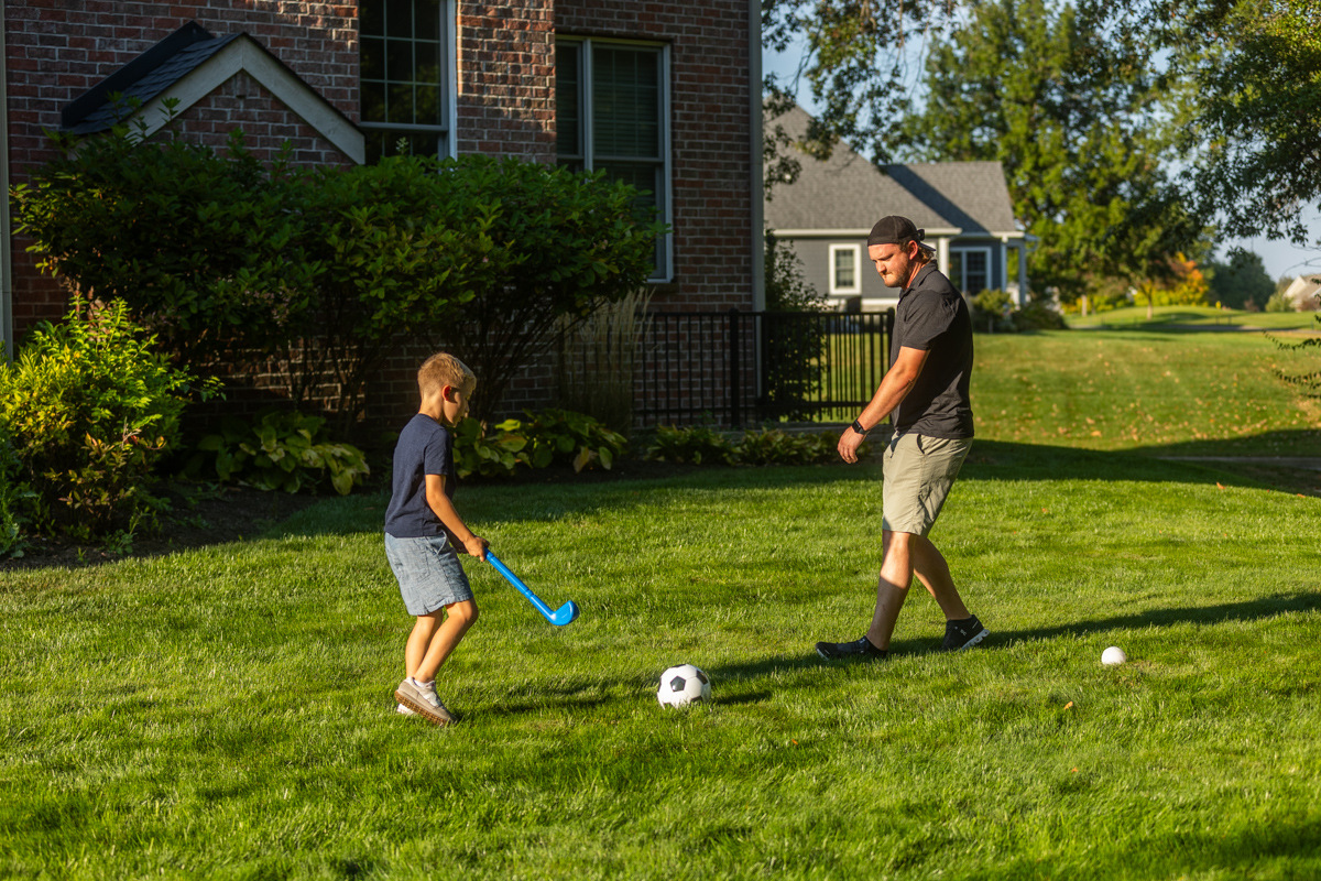 Father and young son playing with a soccer ball on a backyard lawn