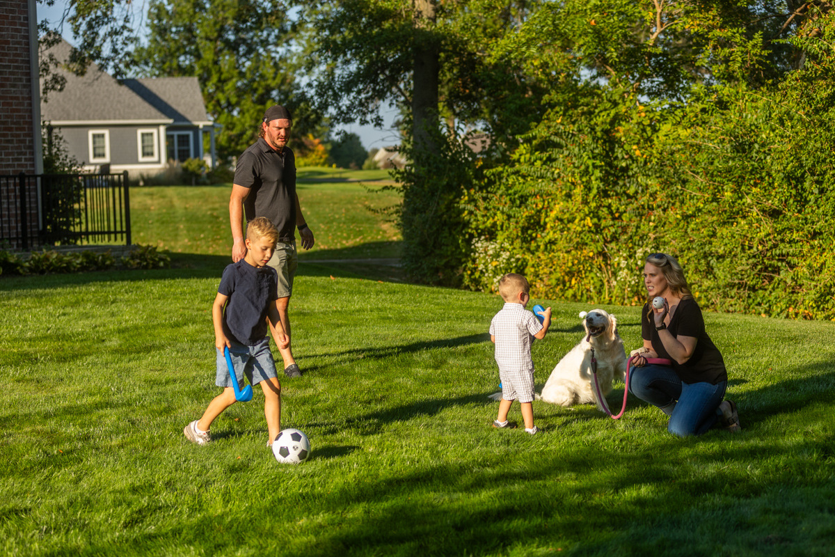 Family playing soccer with their white retriever on a green backyard lawn