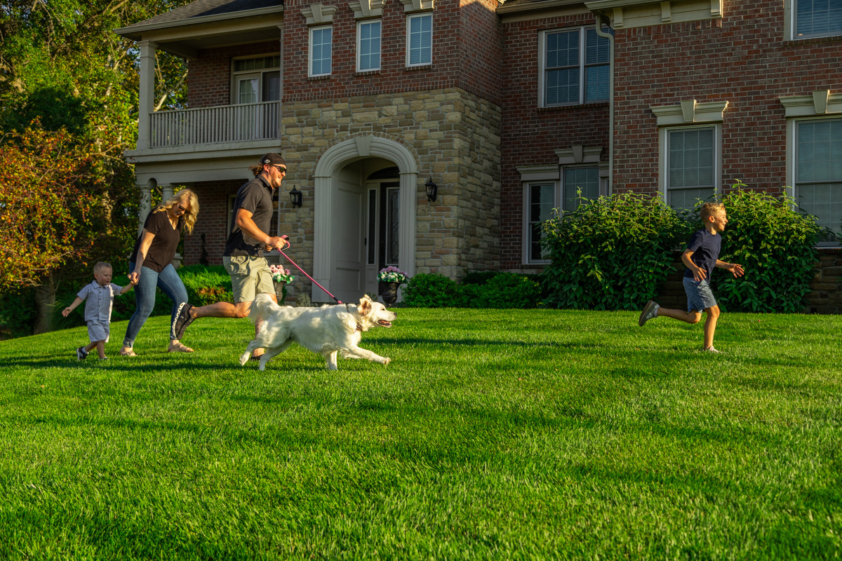 Family and their white retriever running across the front lawn of a brick home