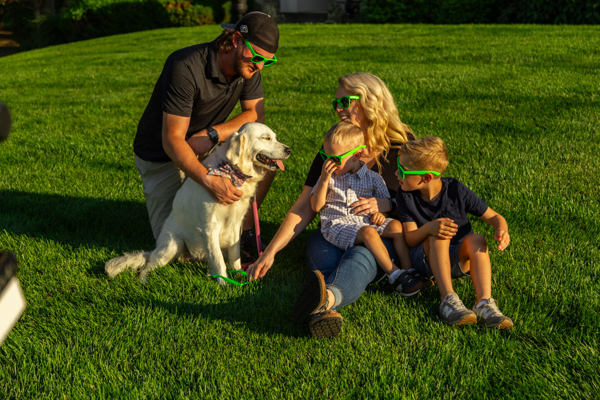 Family in green novelty glasses petting their white retriever on the lawn