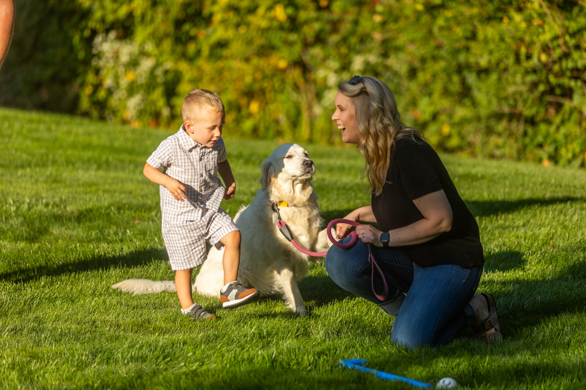 Mother and toddler crouching beside a white retriever on a green lawn