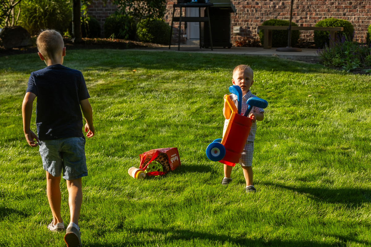 Two young boys playing with toys on a green backyard lawn