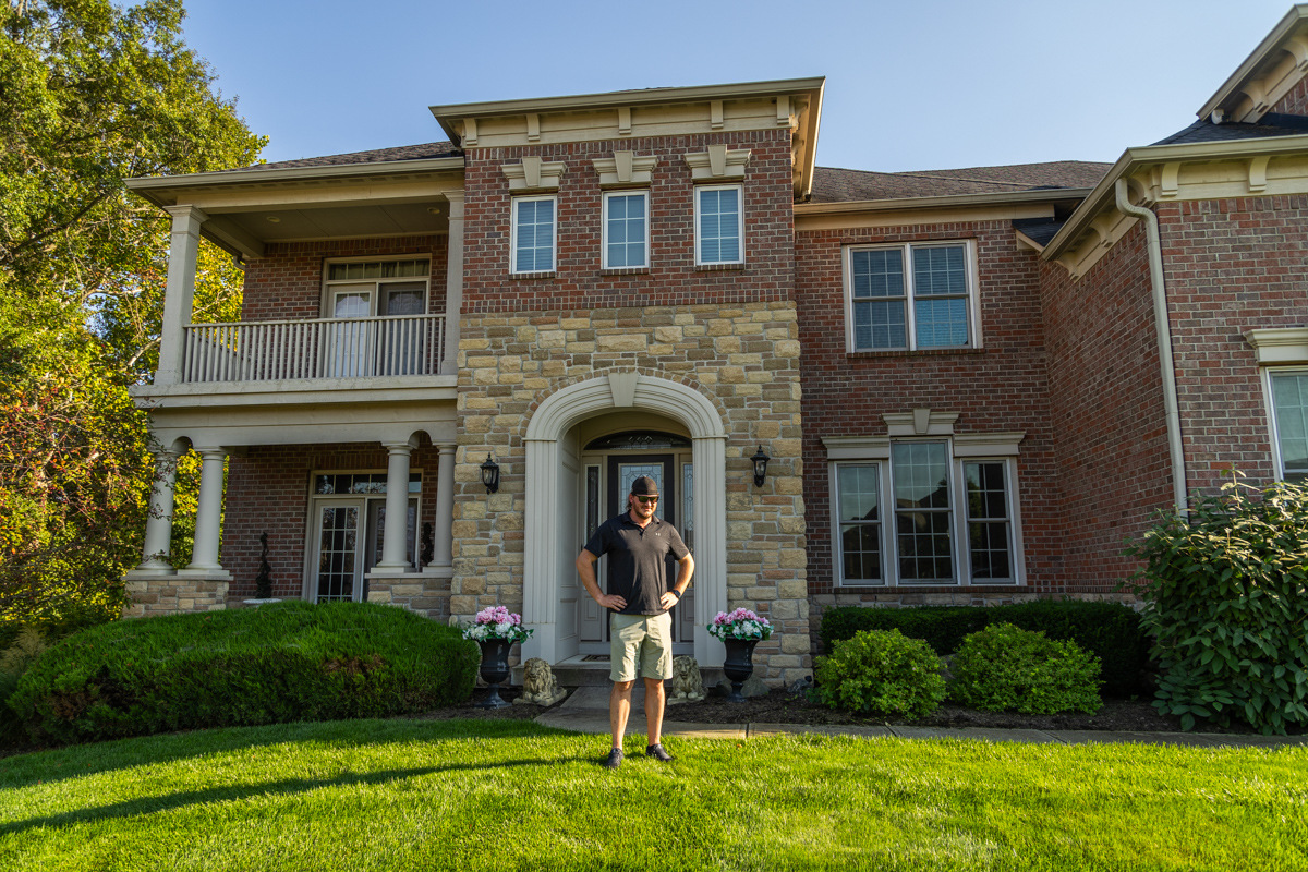 Homeowner standing on a green lawn in front of a two-story brick and stone house