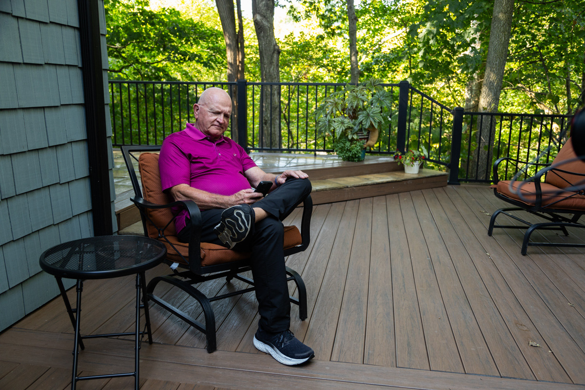 Older man in a magenta polo checking his phone on a backyard deck