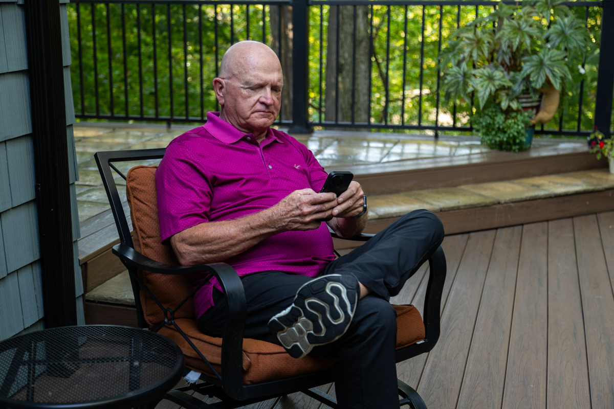 Man in a magenta polo reading his phone in a patio chair