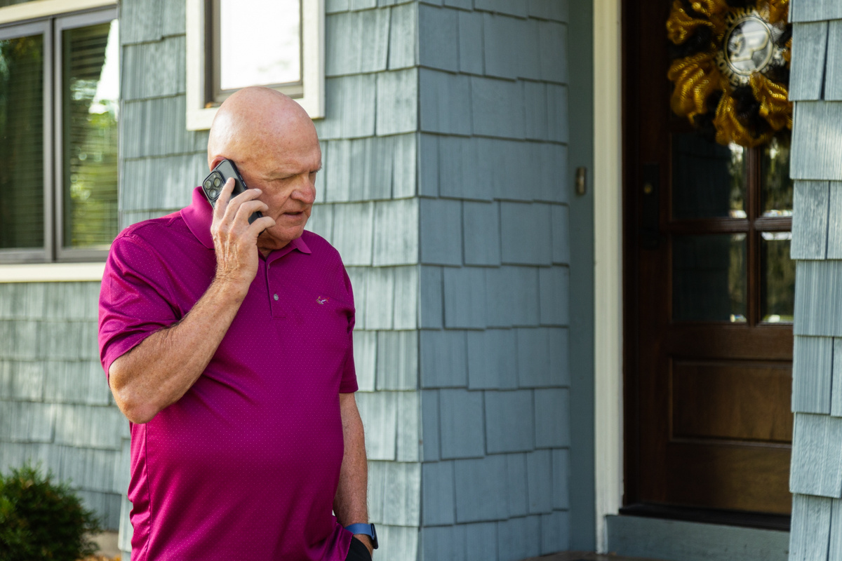 Man in a magenta polo on a phone call outside his front door