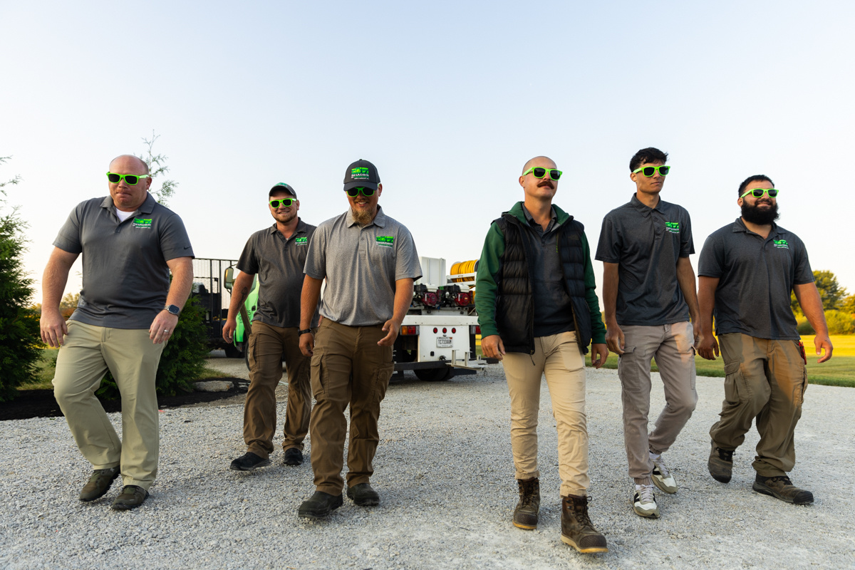 Six Shades of Green crew members in green sunglasses walking across a gravel lot