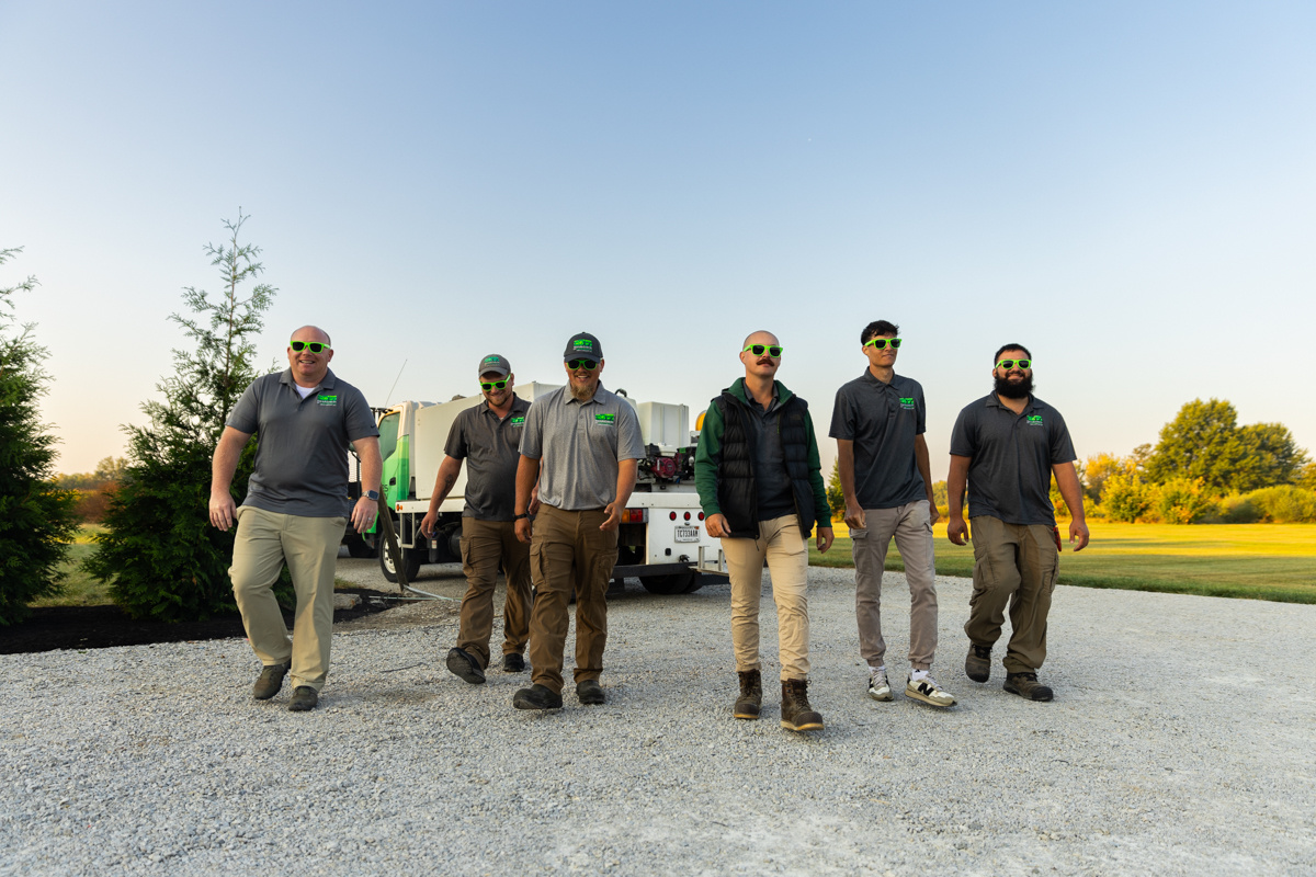 Six Shades of Green crew members walking down a gravel drive at sunset, service trucks behind