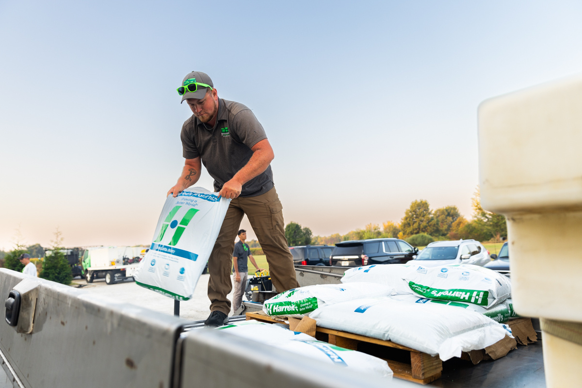 Technician unloading bags of Harrell's fertilizer from a pallet on a truck bed