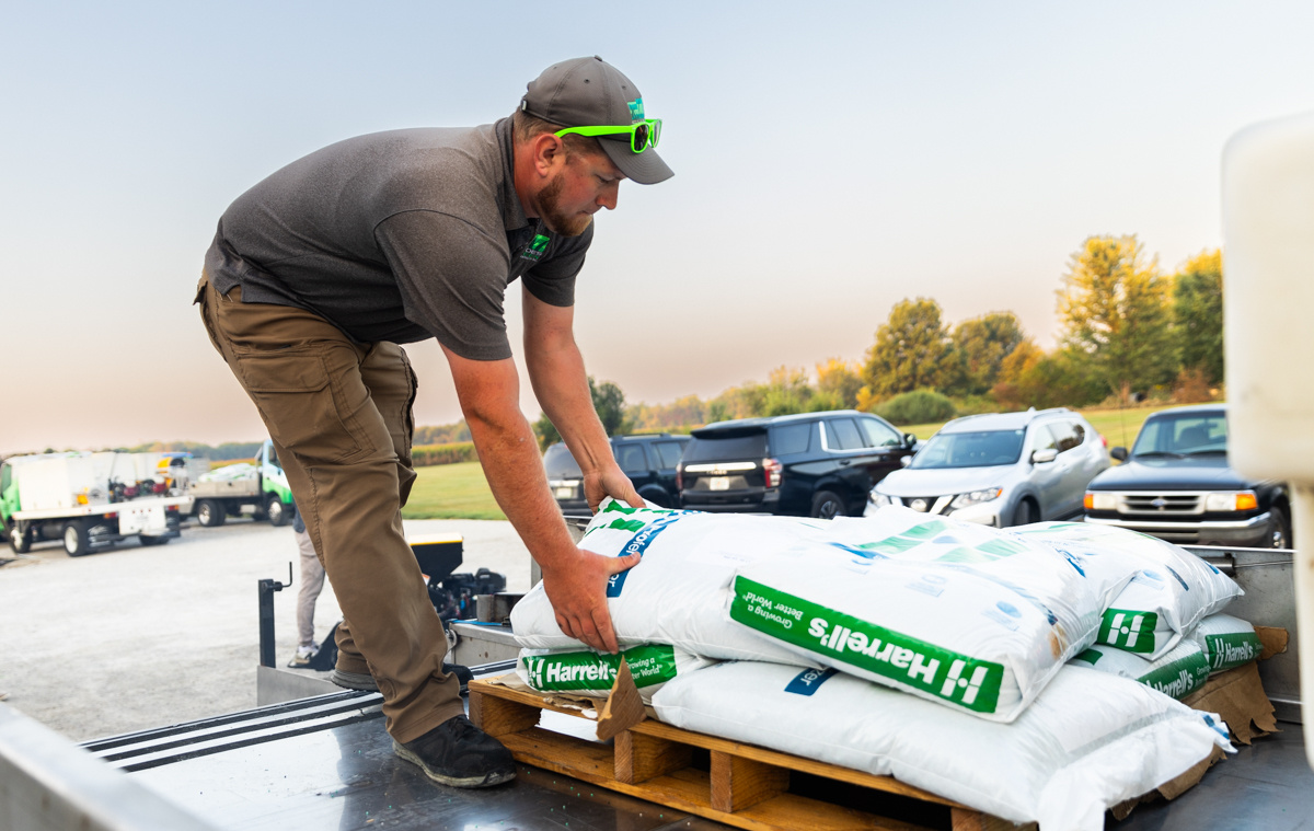 Technician in green sunglasses lifting a bag of Harrell's fertilizer off a pallet