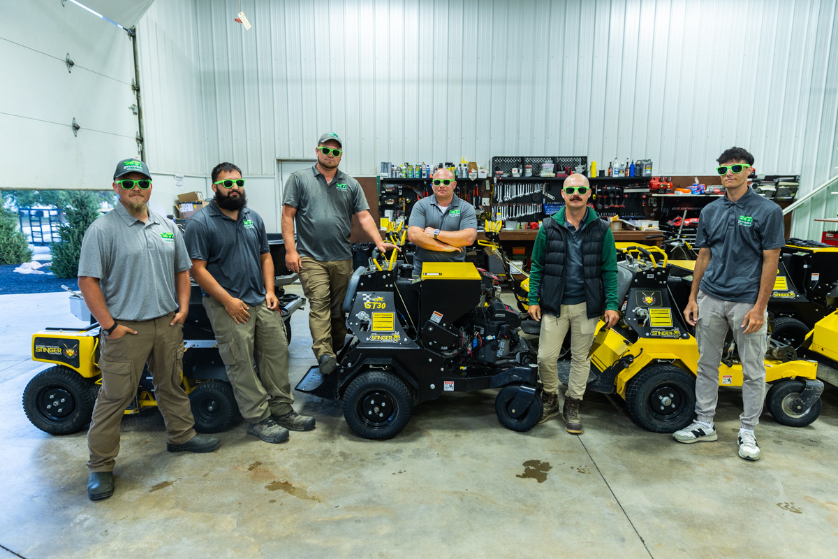 Shades of Green crew in green sunglasses with ride-on lawn equipment in their shop