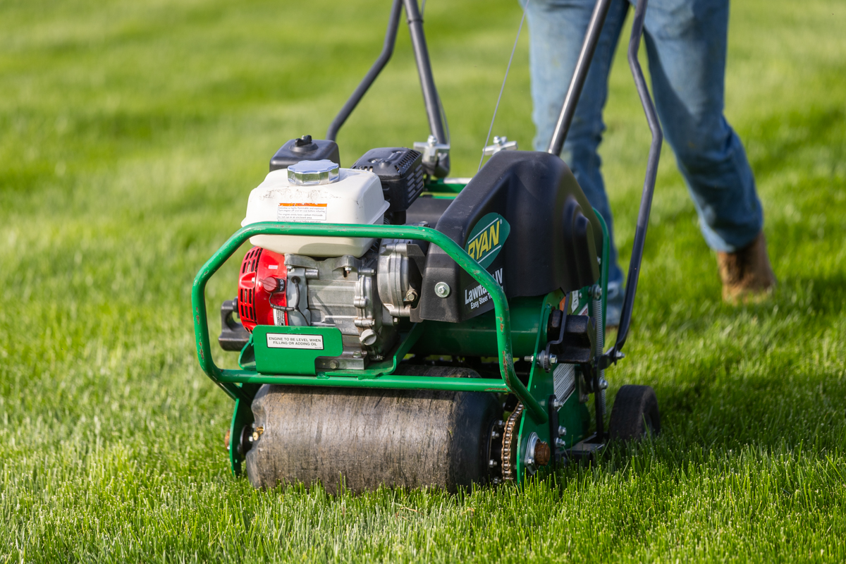Homeowner pushing a walk-behind core aerator across a lawn