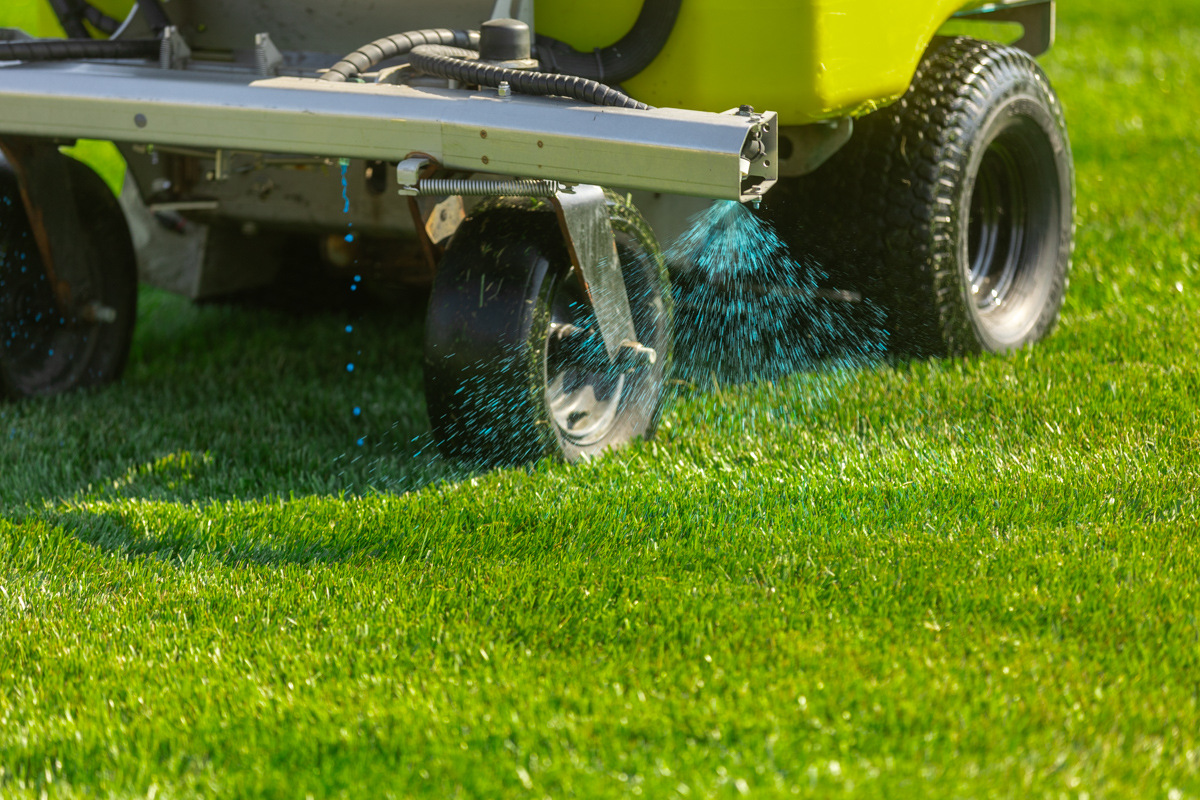 Ride-on sprayer applying a blue-dyed liquid weed control treatment to a green lawn