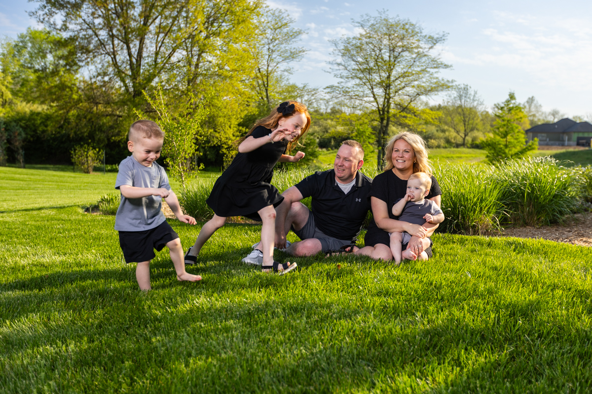 Family with three young children playing on a green backyard lawn