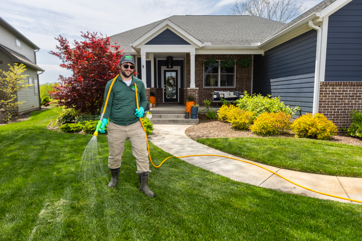 Technician in green sunglasses spraying a front lawn from a hose line