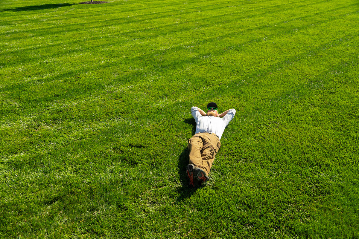 Person lying on their back in the middle of a wide, striped green lawn