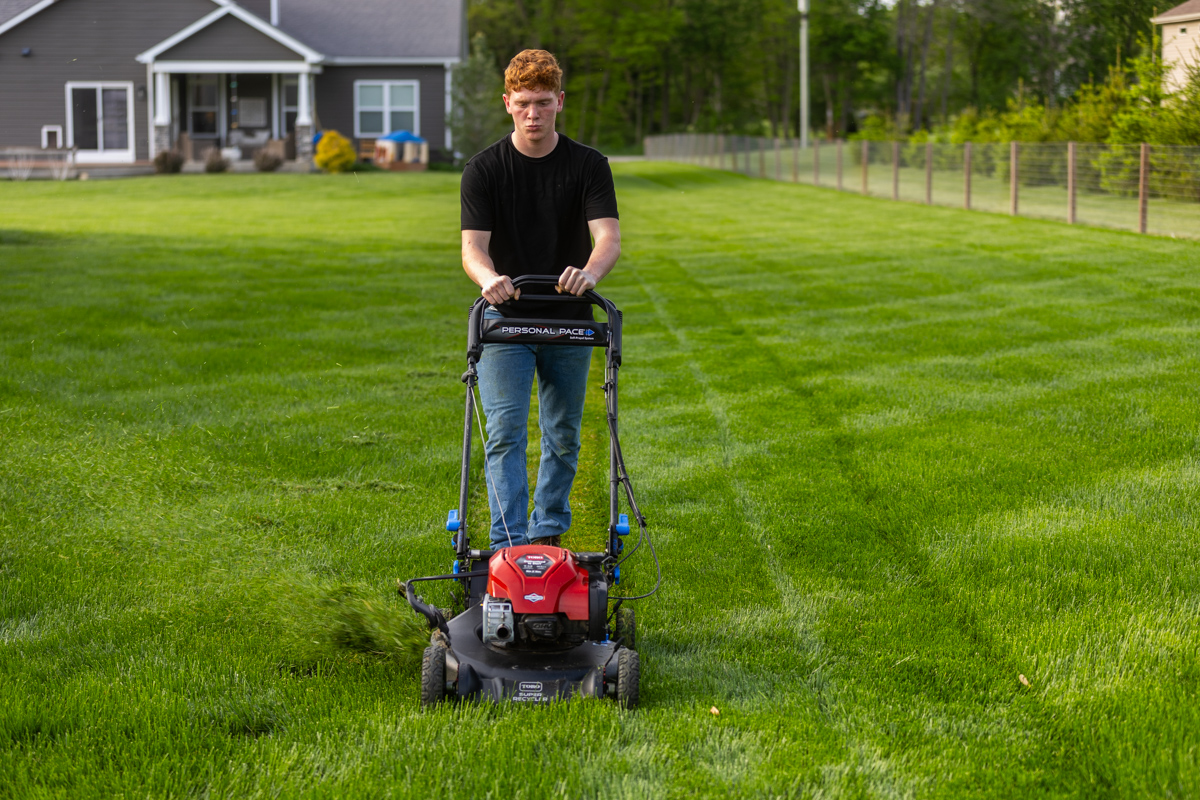 Homeowner pushing a mower toward the camera, leaving stripes in a backyard lawn