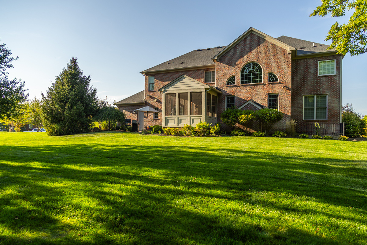 Large brick home with a screened porch behind a wide, sunlit green lawn